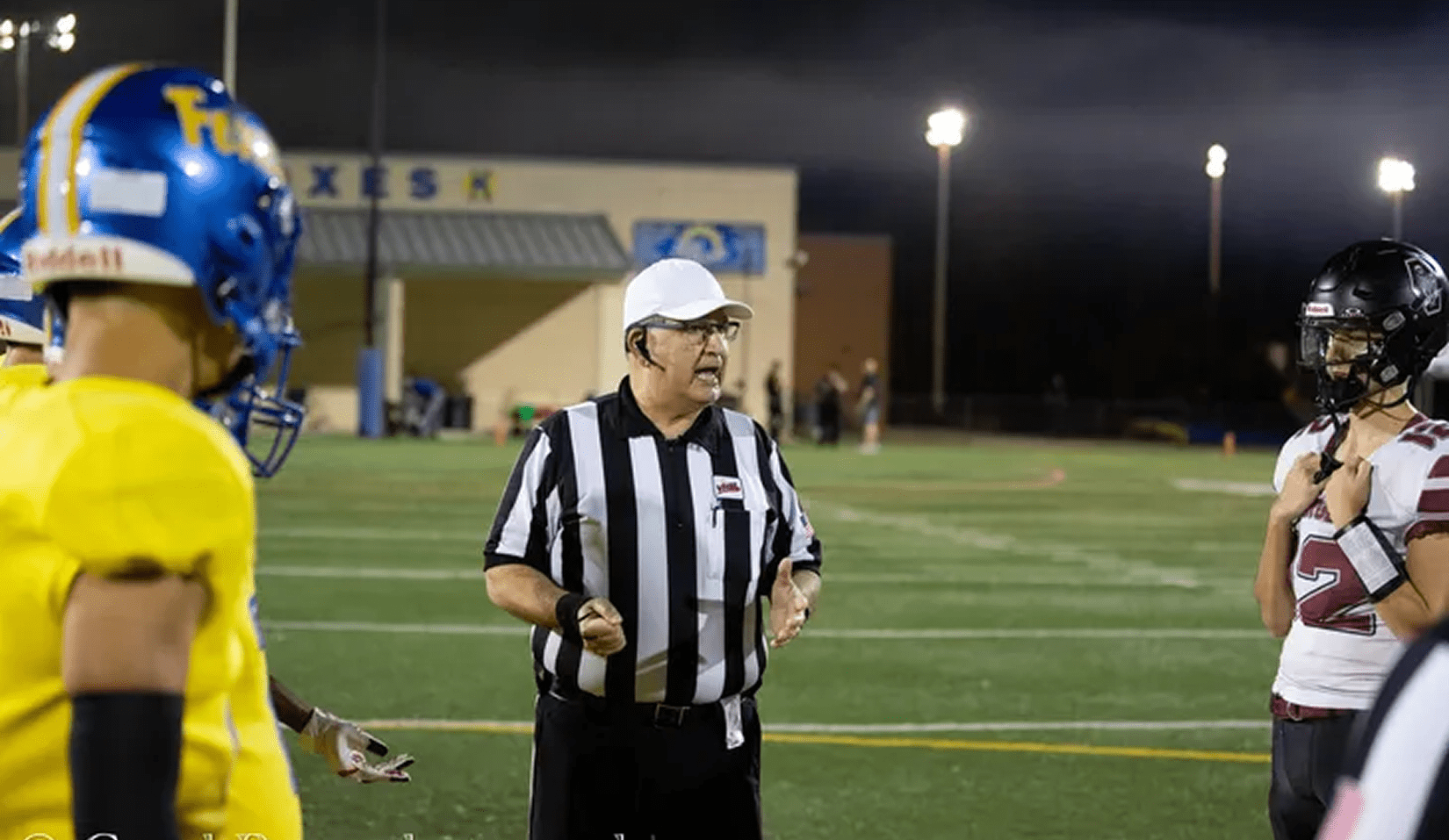 Football referee with players under stadium lights.