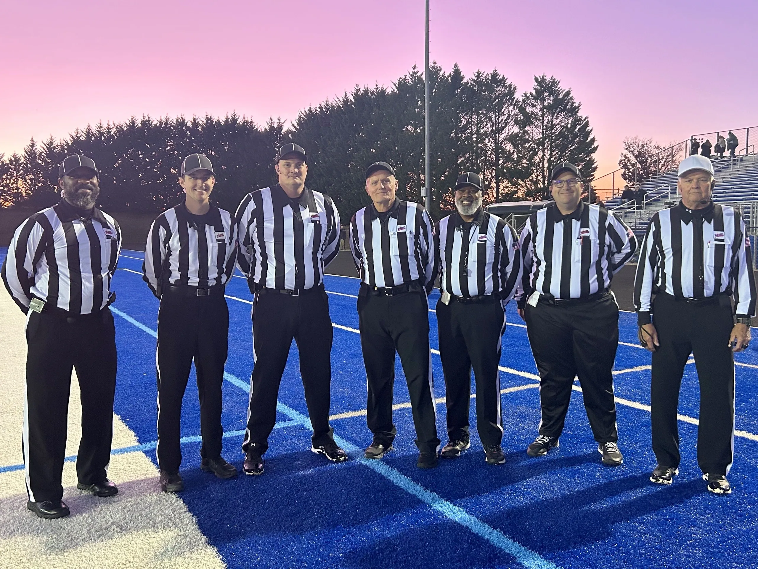 Football referees on blue field at sunset.