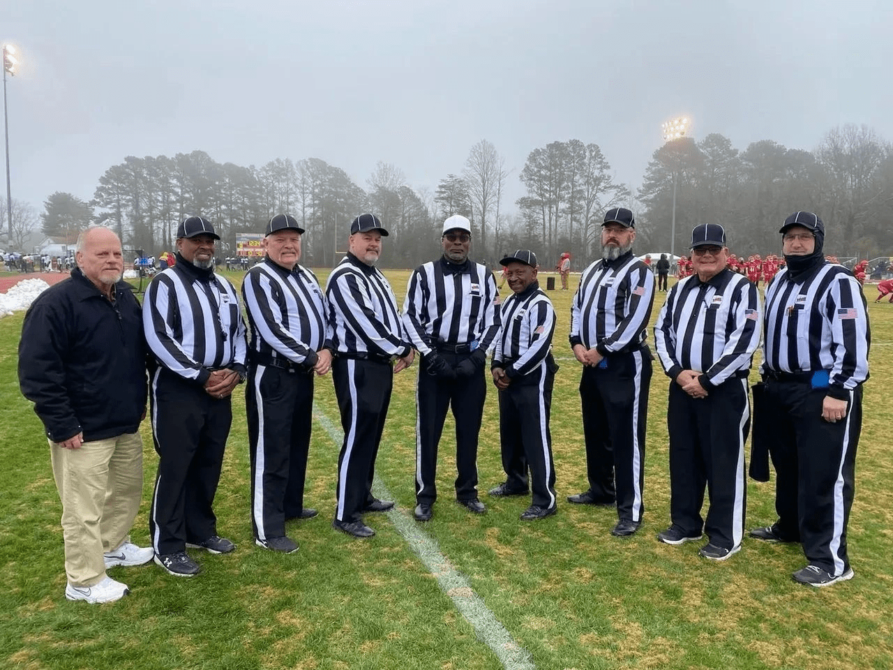 Six referees in striped uniforms standing on a foggy football field.